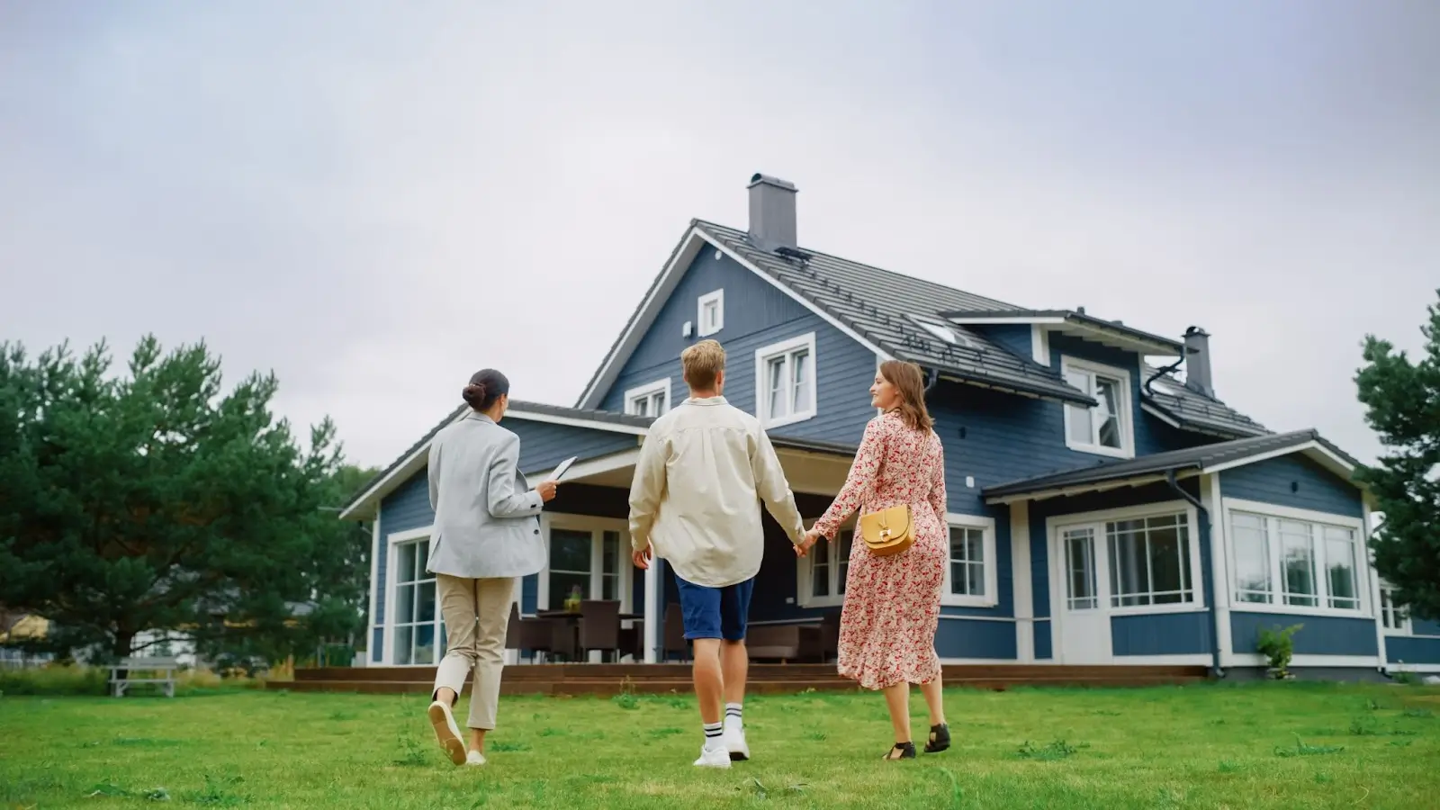 couple and real estate agent walking towards blue house